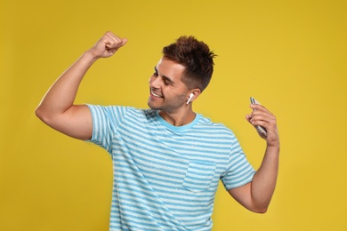 Happy young man with smartphone listening to music through wireless earphones on yellow background