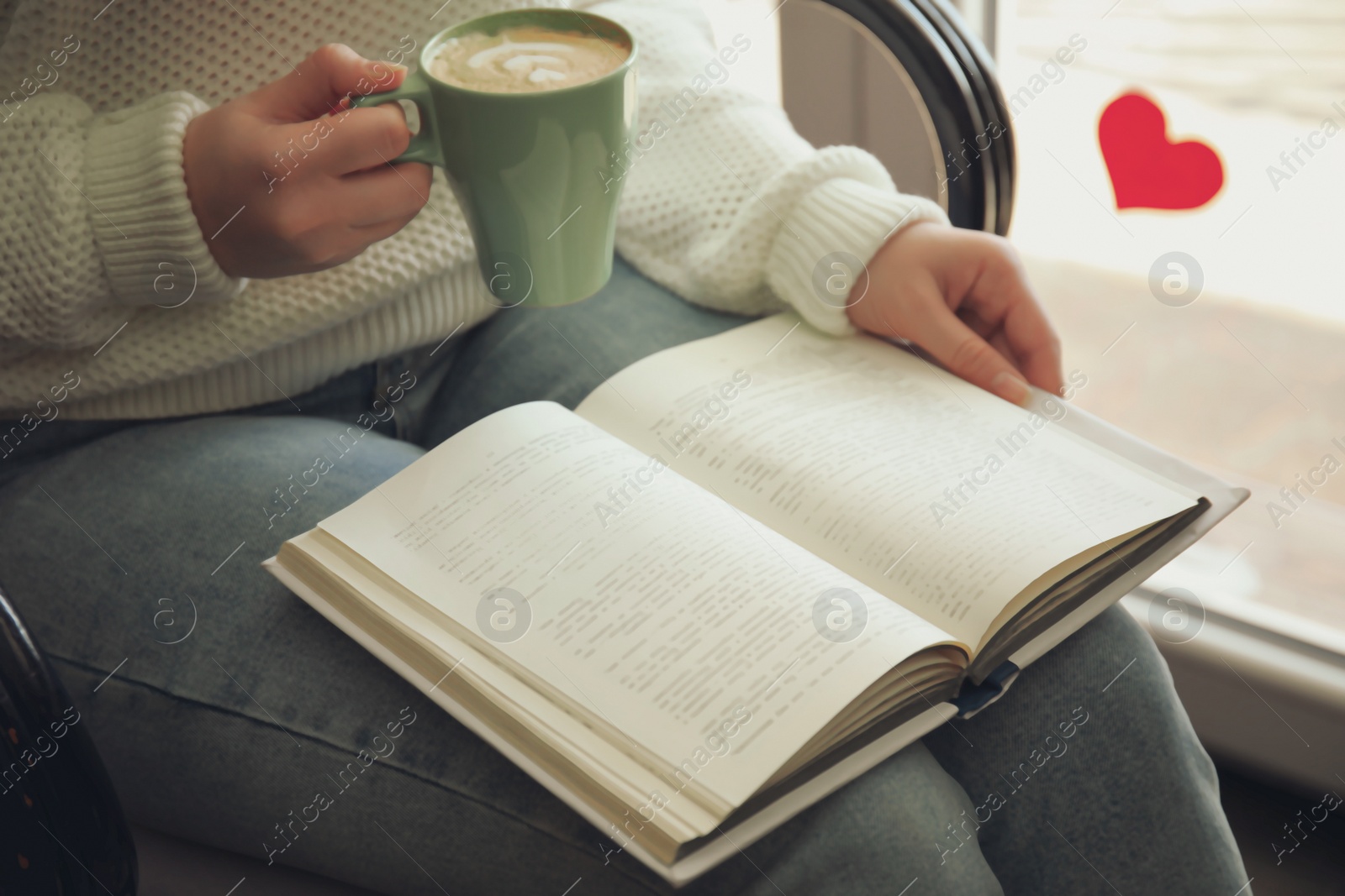 Photo of Woman with cup of coffee reading book indoors, closeup