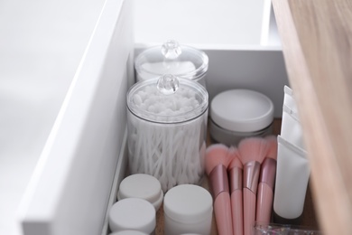 Photo of Cotton buds, pads, creams and makeup brushes in open drawer