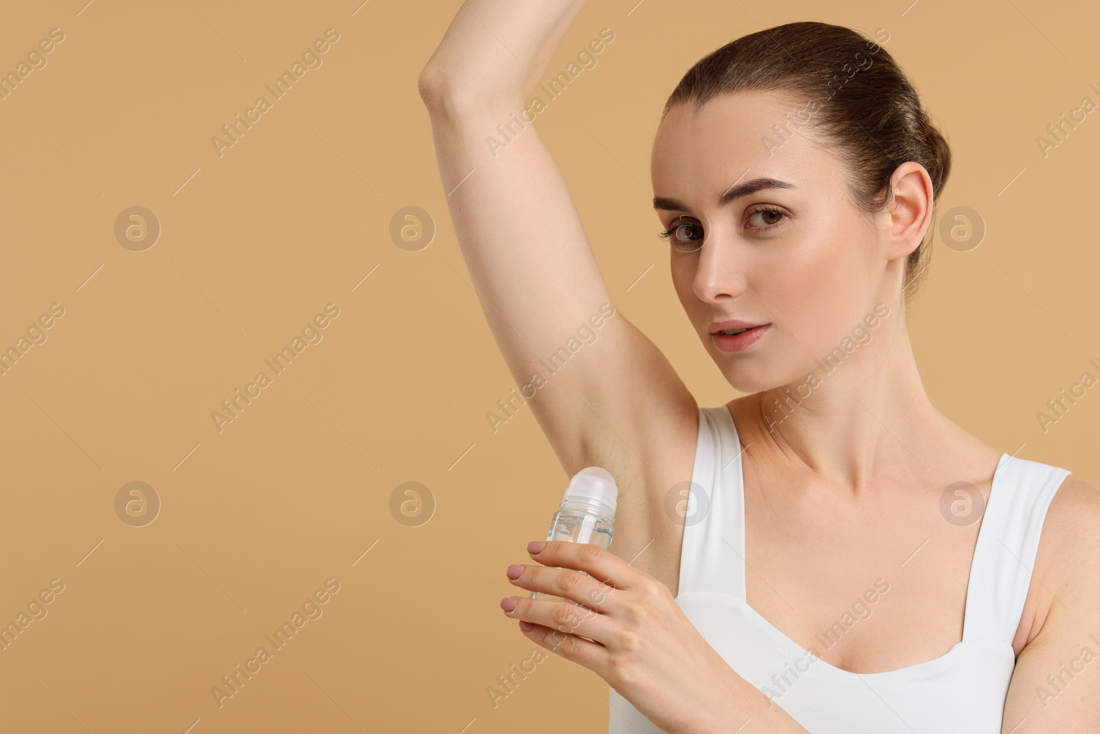 Photo of Beautiful woman applying deodorant on beige background, space for text