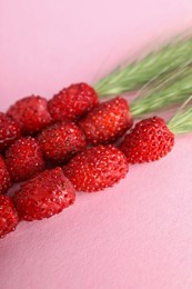 Photo of Grass stems with wild strawberries on pink table, closeup