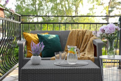 Rattan table with jug of water, glasses and beautiful flowers on terrace