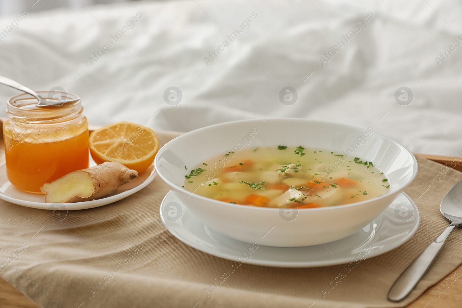 Photo of Tray with bowl of fresh homemade soup to cure flu on bed