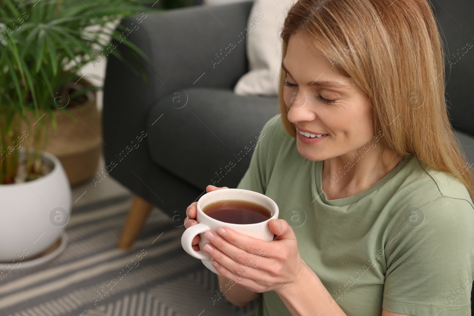 Photo of Woman holding cup of tea in room with beautiful houseplants. Space for text