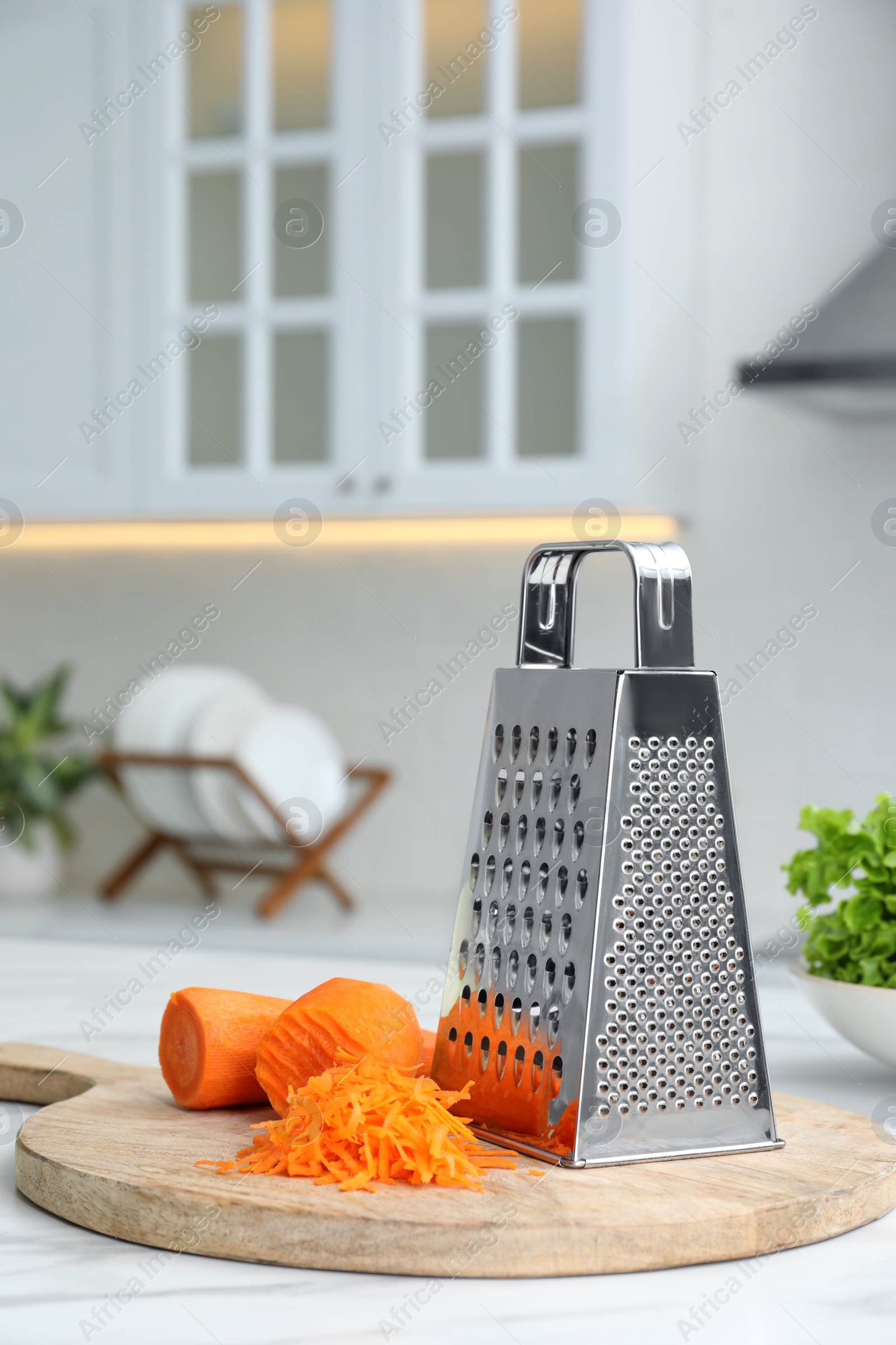 Photo of Grater and fresh ripe carrot on white table in kitchen. Space for text