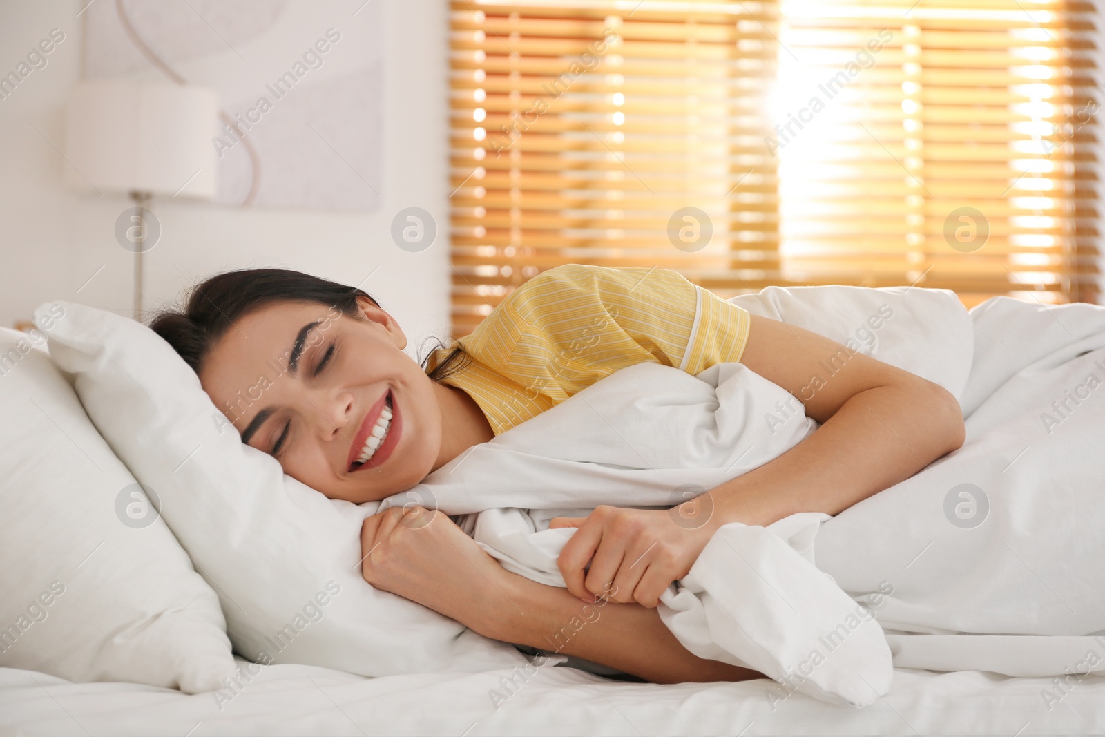 Photo of Young woman lying in bed with white linens at home