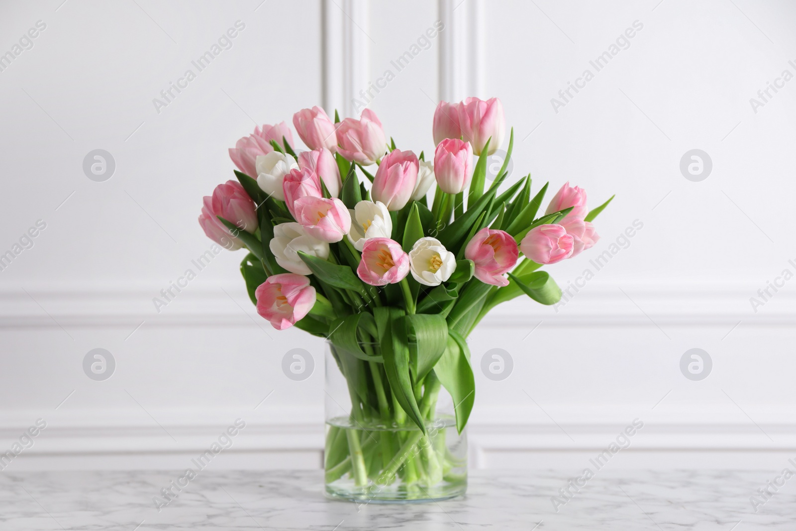 Photo of Beautiful bouquet of tulips in glass vase on white marble table