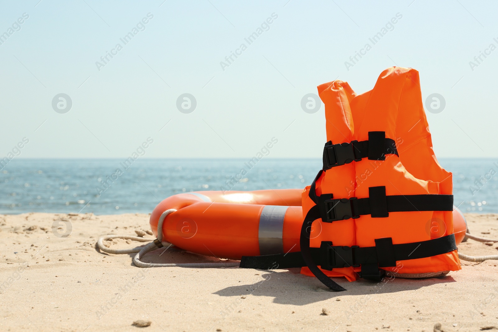 Photo of Orange life jacket and buoy on sandy beach near sea. Emergency rescue equipment