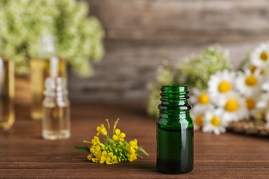 Photo of Bottle of essential oil with flowers on wooden table, space for text
