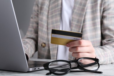 Photo of Online payment. Woman with laptop and credit card at white marble table, closeup