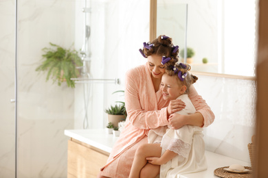 Photo of Happy mother and daughter with curlers in bathroom