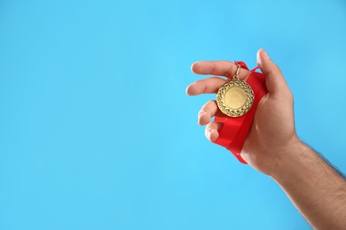 Photo of Man holding golden medal on light blue background, closeup. Space for design