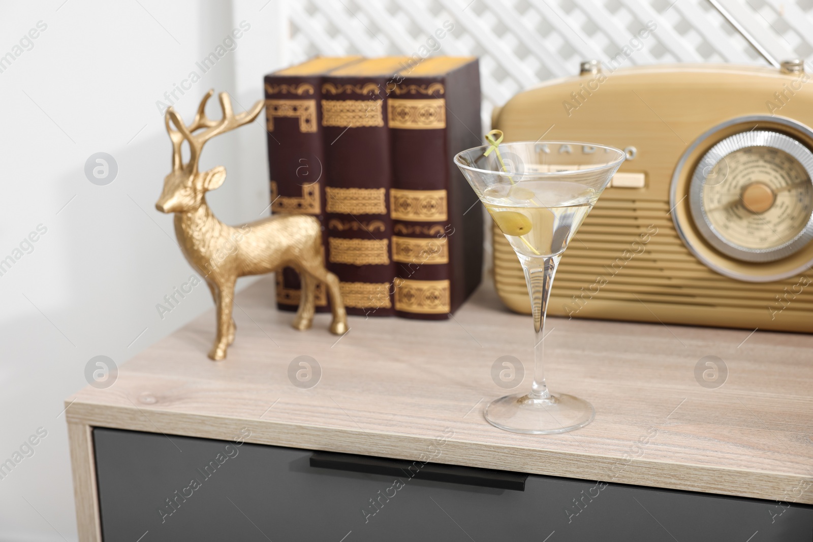 Photo of Martini cocktail with olive, retro radio receiver and decor on wooden table in room. Relax at home