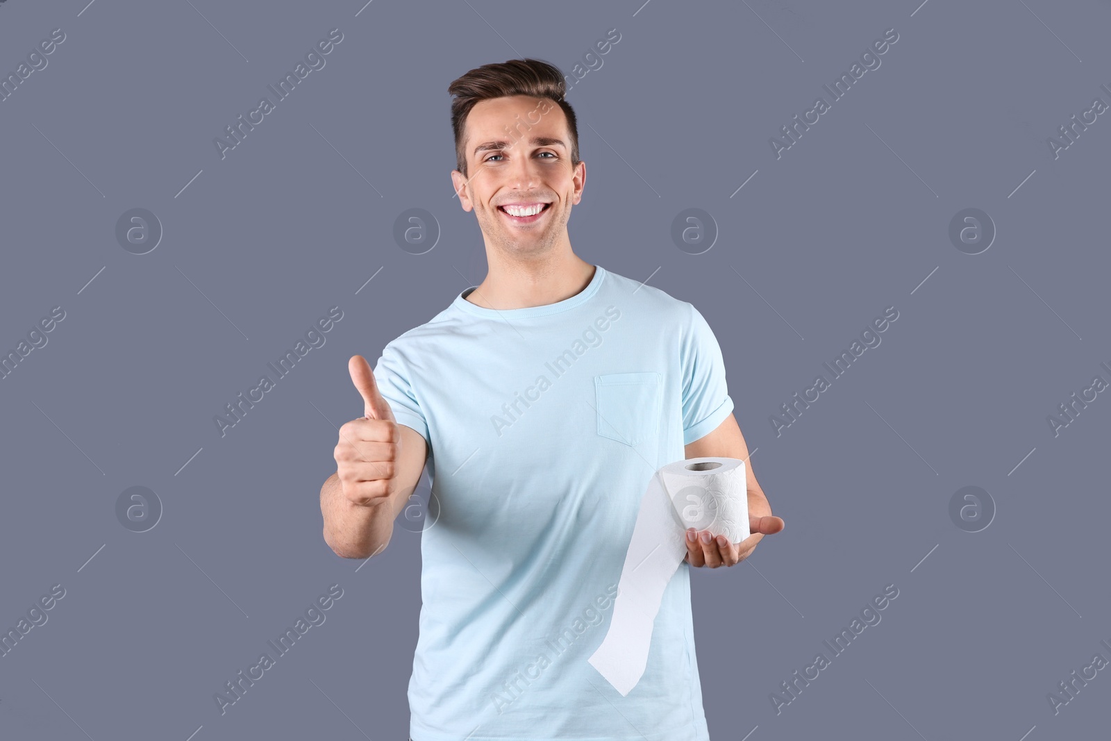 Photo of Young man holding toilet paper roll on color background