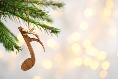 Photo of Fir tree branch with wooden note against blurred lights, space for text. Christmas music