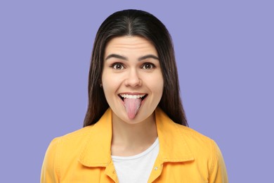 Photo of Happy young woman showing her tongue on purple background