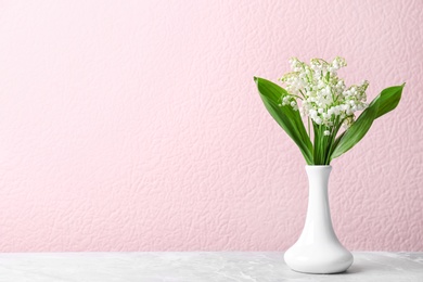 Photo of Beautiful lily of the valley bouquet in vase on table near color wall, space for text