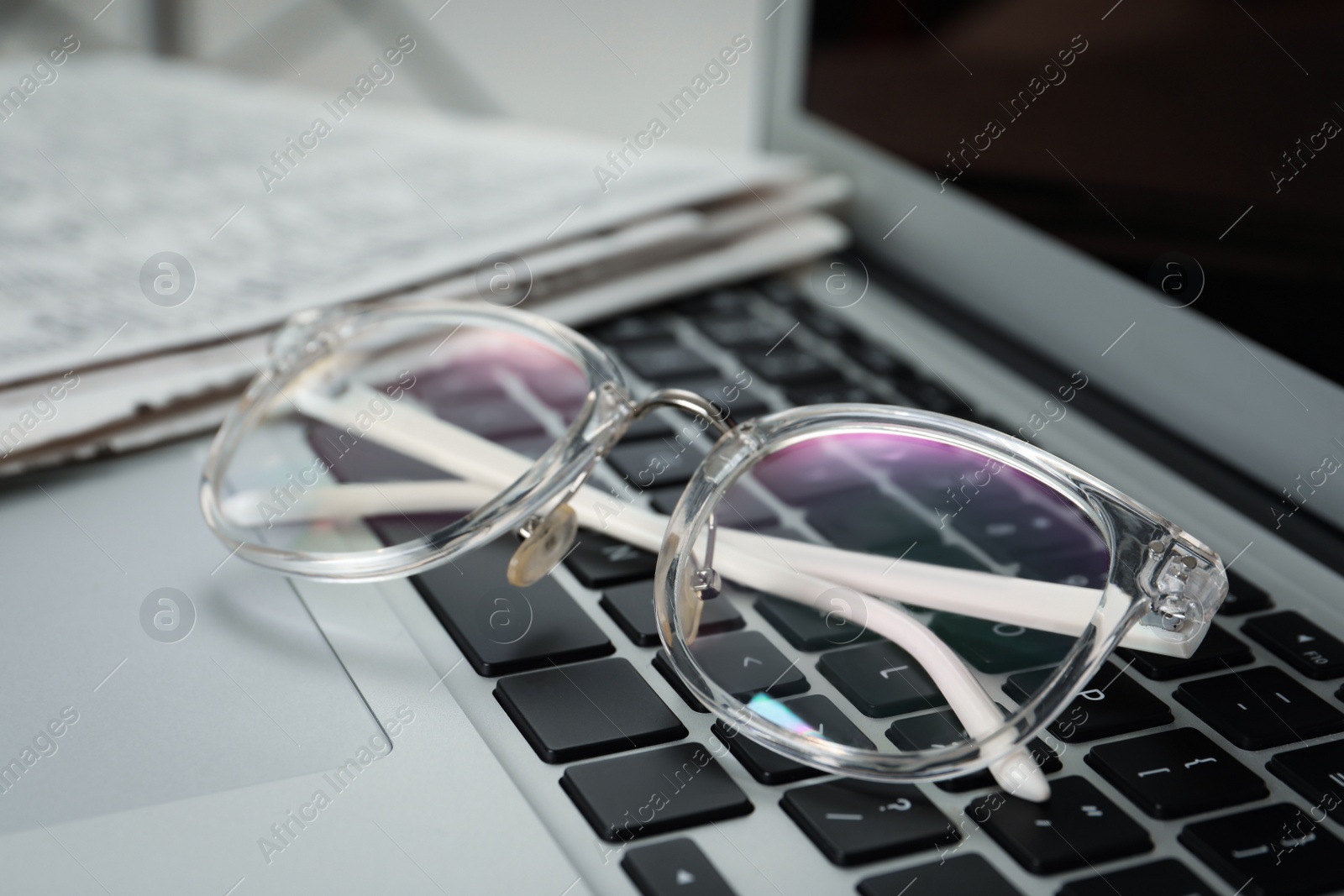 Photo of Glasses and newspapers on modern laptop, closeup