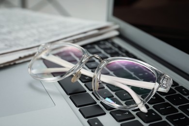 Glasses and newspapers on modern laptop, closeup