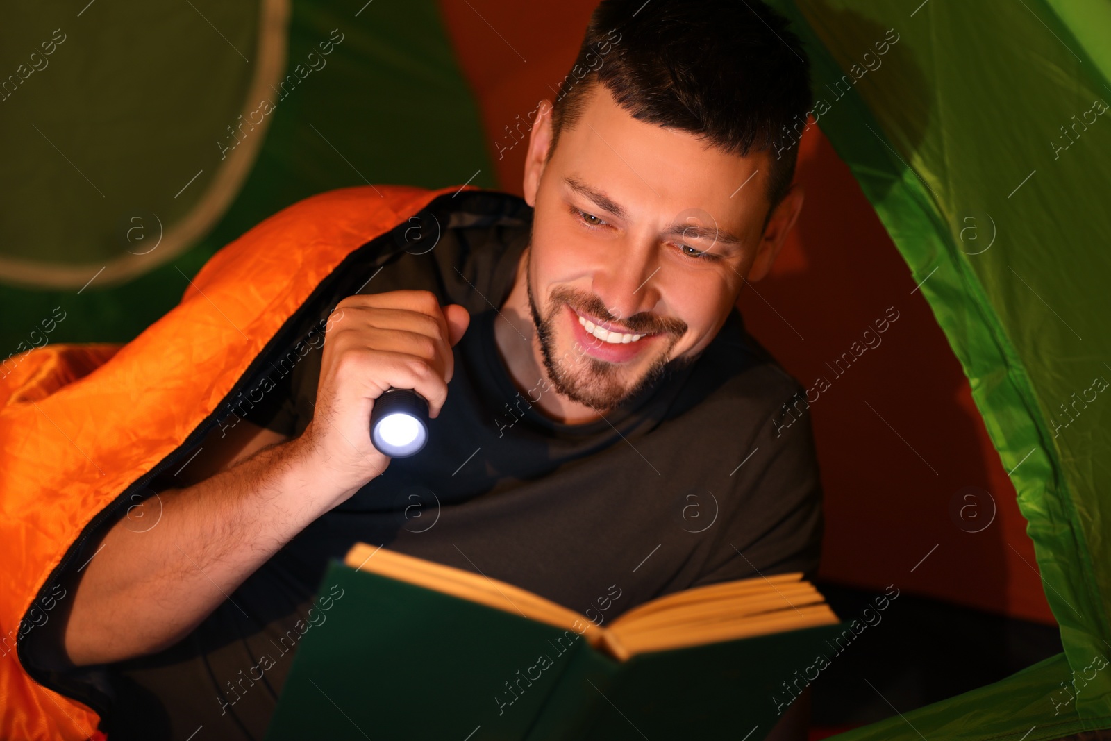 Photo of Man with flashlight reading book in tent