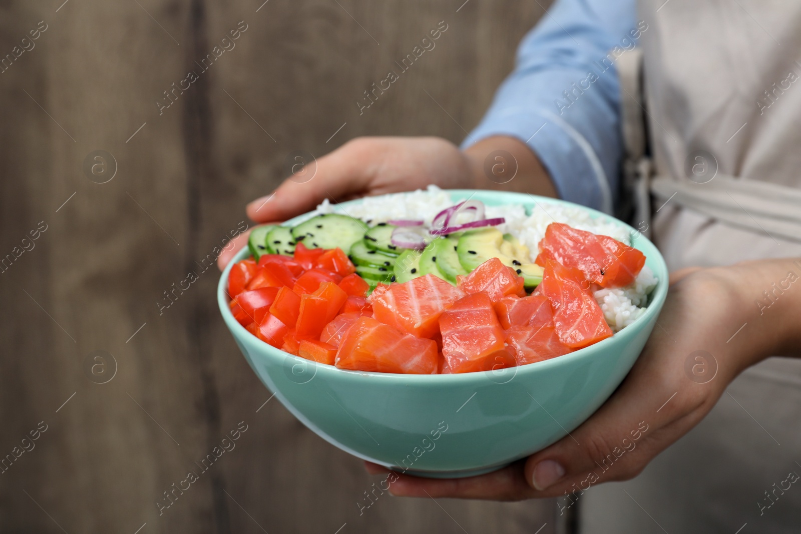 Photo of Woman holding delicious poke bowl with salmon and vegetables against wooden background, closeup