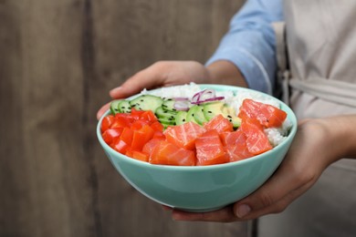 Woman holding delicious poke bowl with salmon and vegetables against wooden background, closeup