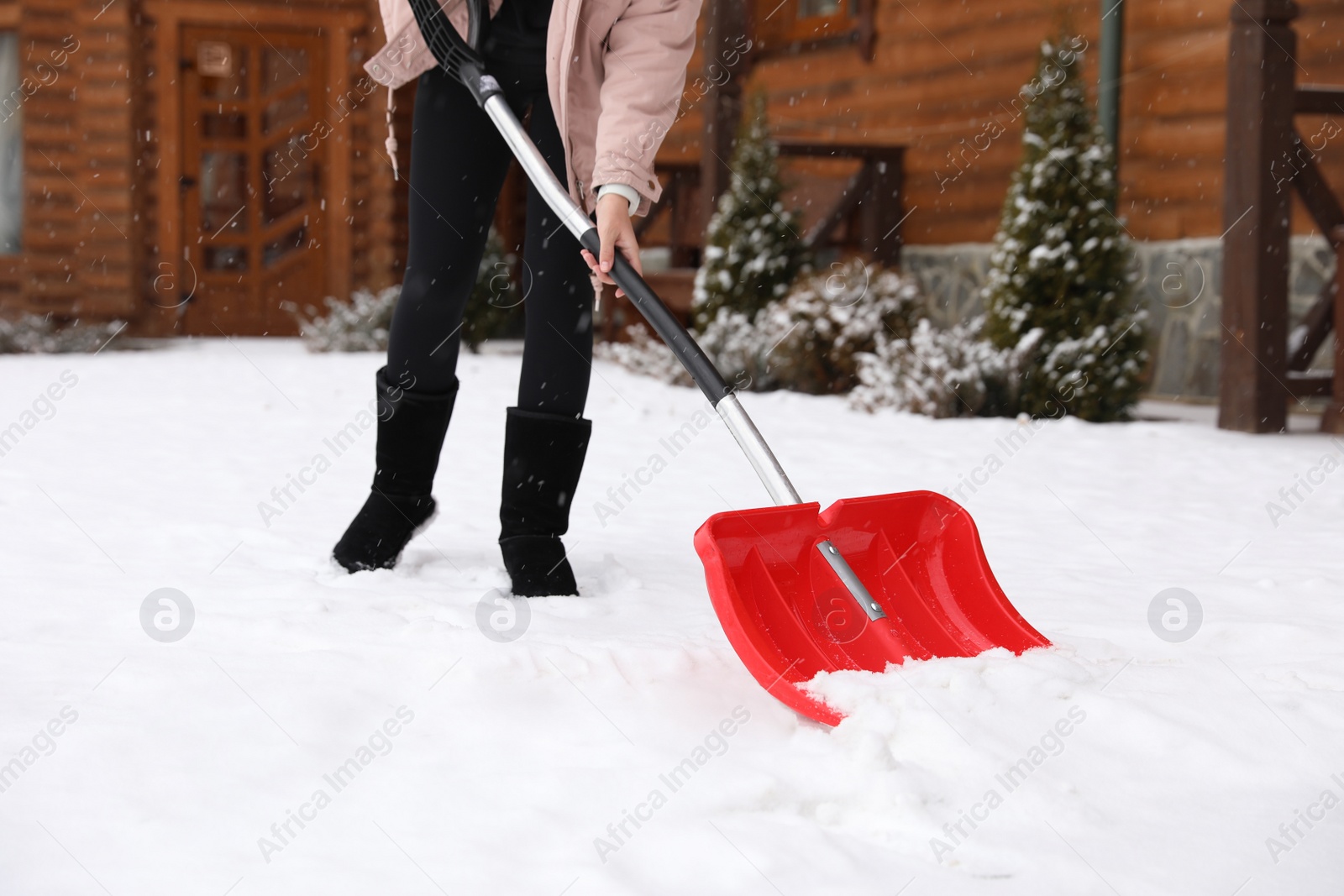 Photo of Young woman cleaning snow with shovel near her house