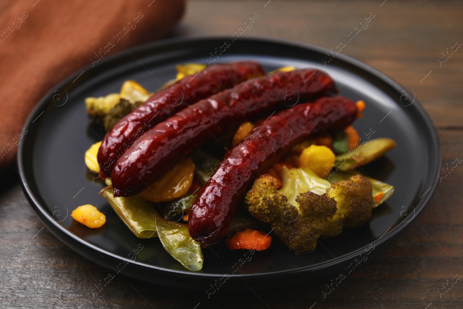 Photo of Delicious smoked sausages and baked vegetables on wooden table, closeup