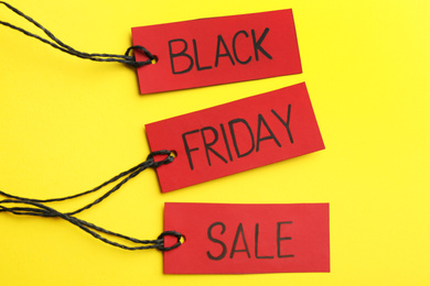 Red tags with words BLACK FRIDAY SALE on yellow background, flat lay