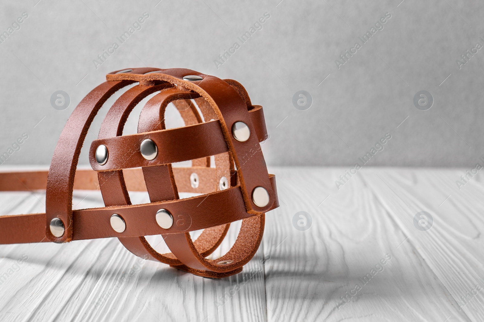 Photo of Brown leather dog muzzle on white wooden table, closeup. Space for text