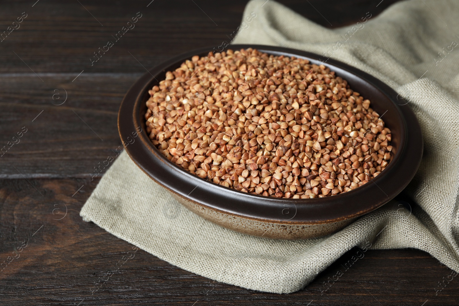 Photo of Uncooked buckwheat in bowl on wooden table