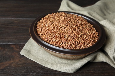 Photo of Uncooked buckwheat in bowl on wooden table