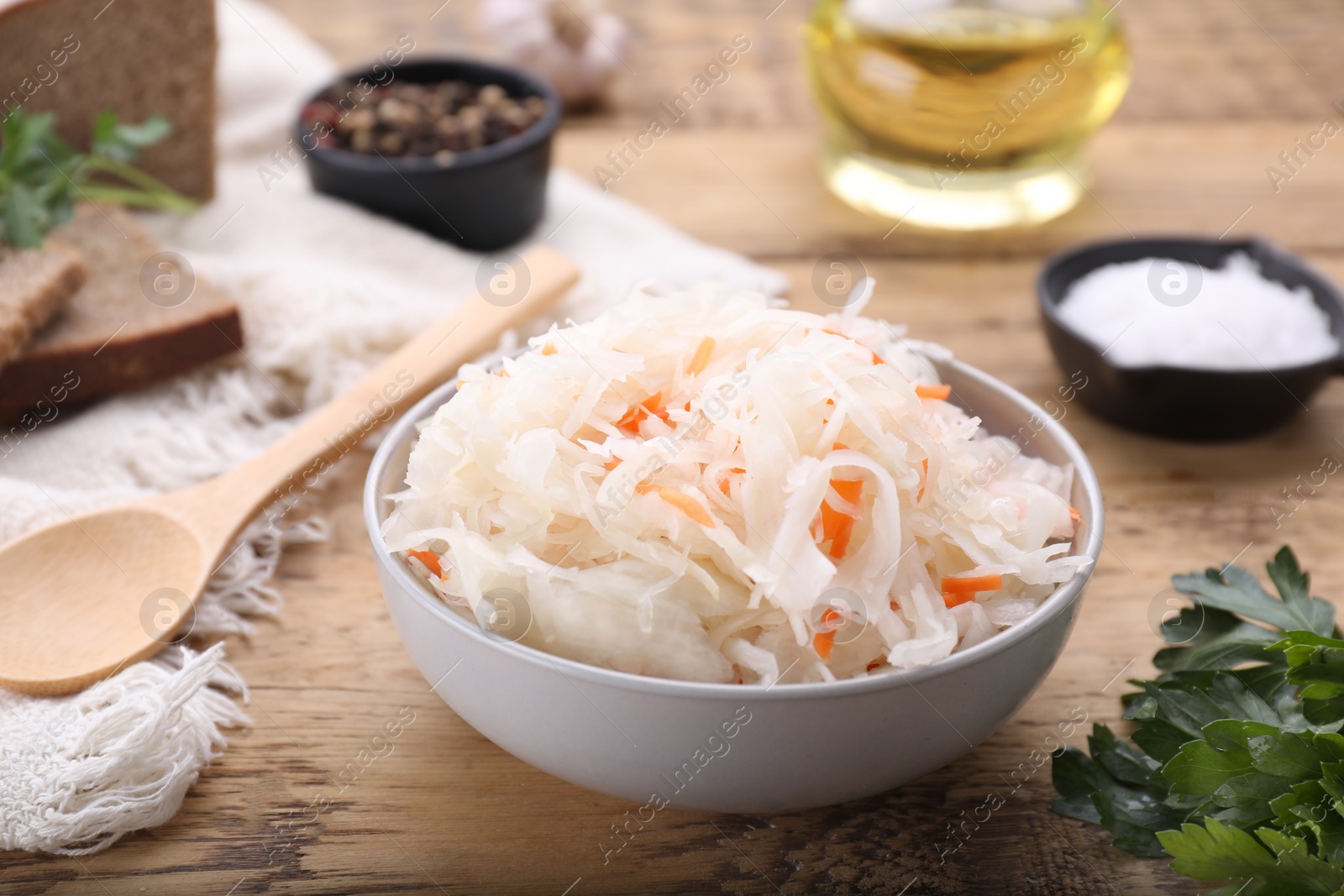 Photo of Bowl of tasty sauerkraut and ingredients on wooden table