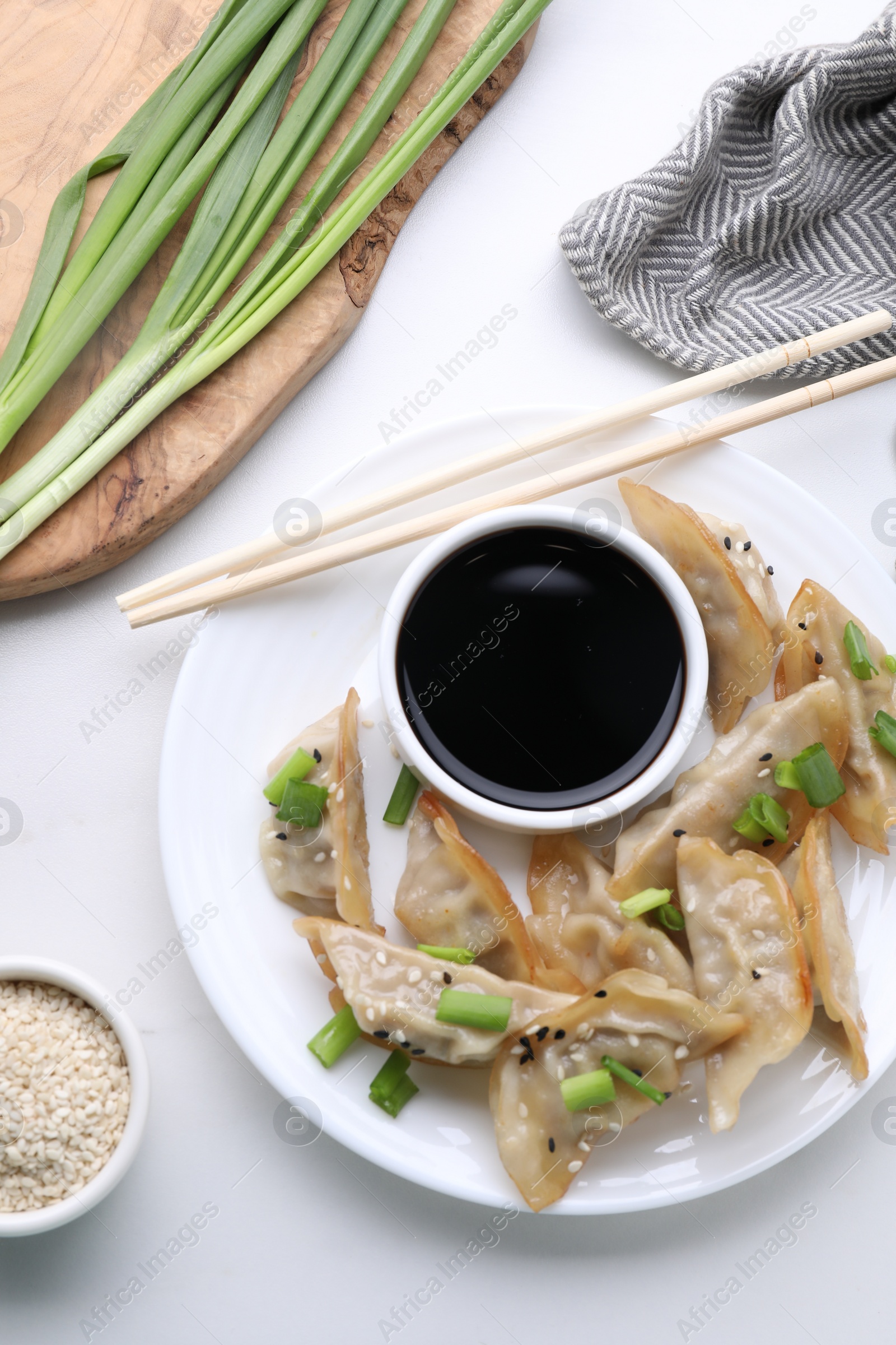 Photo of Delicious gyoza (asian dumplings) with green onions, soy sauce and chopsticks on white table, flat lay