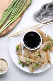 Delicious gyoza (asian dumplings) with green onions, soy sauce and chopsticks on white table, flat lay