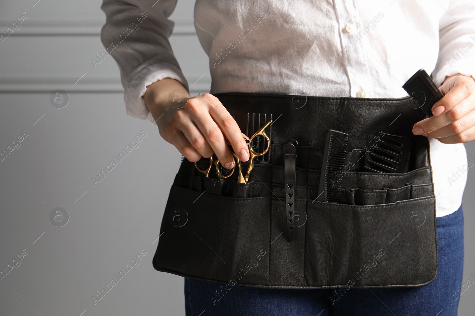 Photo of Hairstylist with professional tools in waist pouch near grey wall, closeup. Space for text