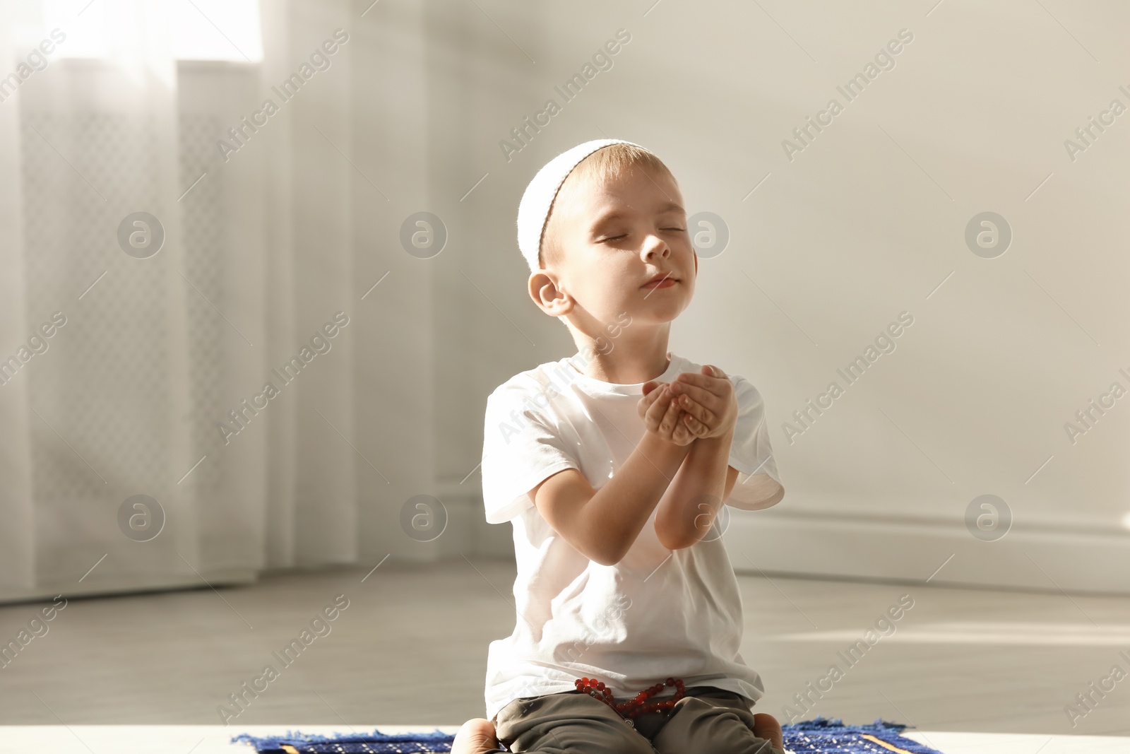 Photo of Little Muslim boy with misbaha praying indoors