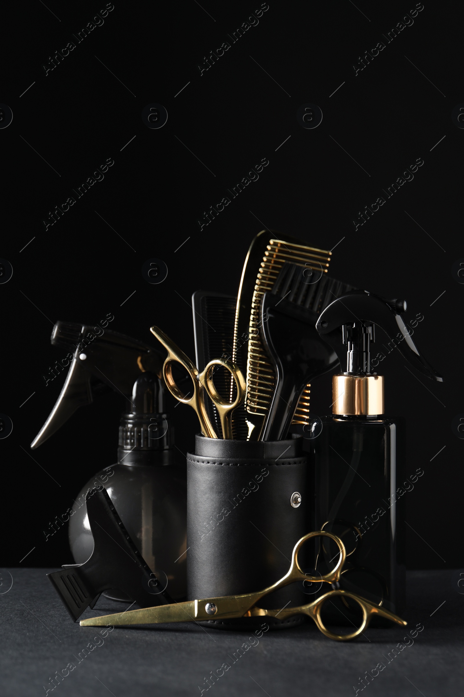 Photo of Different hairdresser tools on grey table against black background