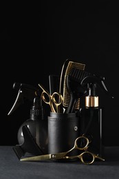 Different hairdresser tools on grey table against black background