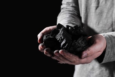 Photo of Man with handful of coal on dark background, closeup. Space for text