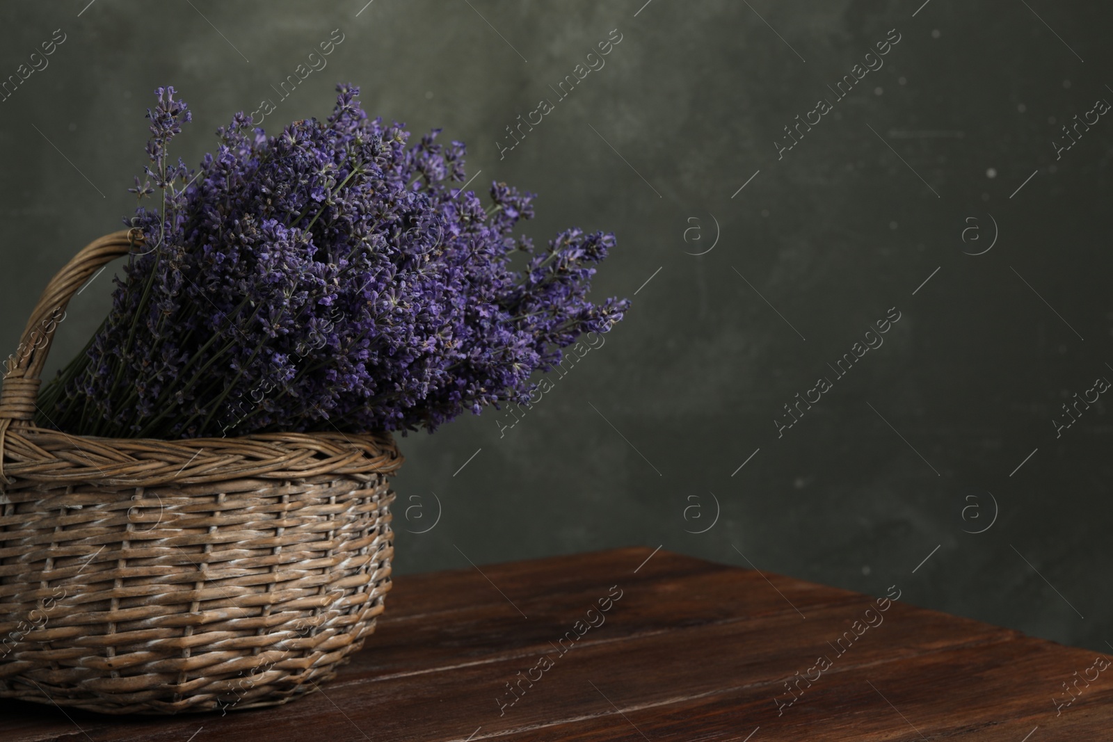 Photo of Beautiful fresh lavender flowers in wicker basket on wooden table against grey background. Space for text