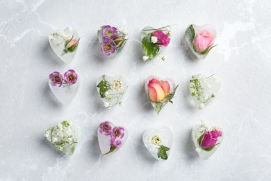 Photo of Heart shaped ice cubes with flowers on grey background, flat lay