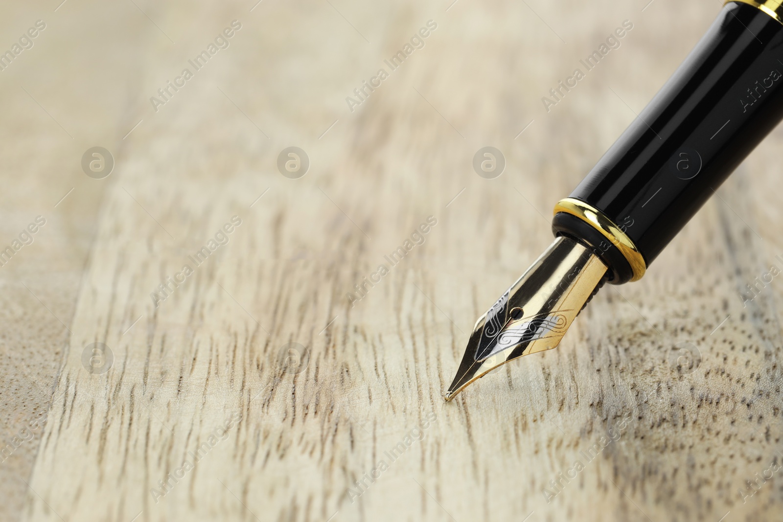 Photo of Stylish fountain pen on wooden table, closeup. Space for text