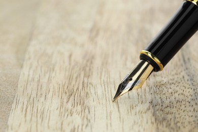 Photo of Stylish fountain pen on wooden table, closeup. Space for text