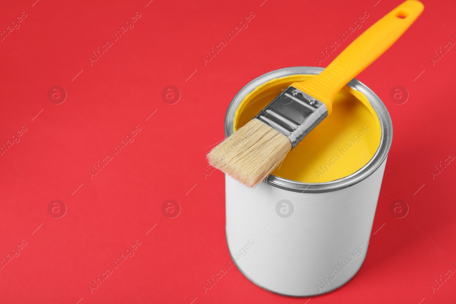 Photo of Can of yellow paint with brush on red background. Space for text