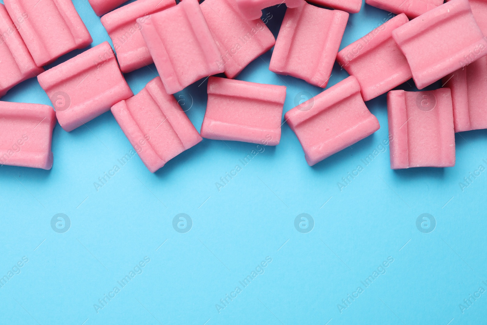 Photo of Tasty pink chewing gums on light blue background, flat lay. Space for text