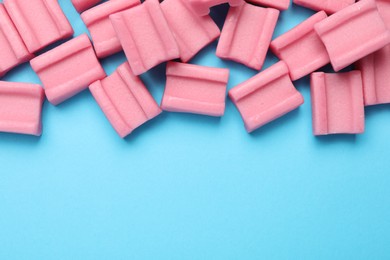 Photo of Tasty pink chewing gums on light blue background, flat lay. Space for text