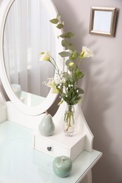 Photo of Beautiful flowers in vase and ceramic fruits on white dressing table