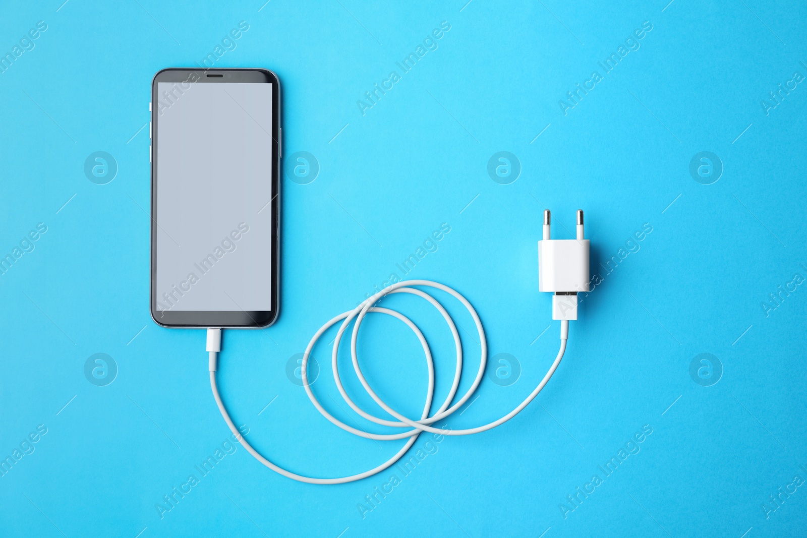 Photo of Smartphone and USB charger on light blue background, flat lay. Modern technology