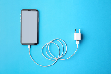 Photo of Smartphone and USB charger on light blue background, flat lay. Modern technology